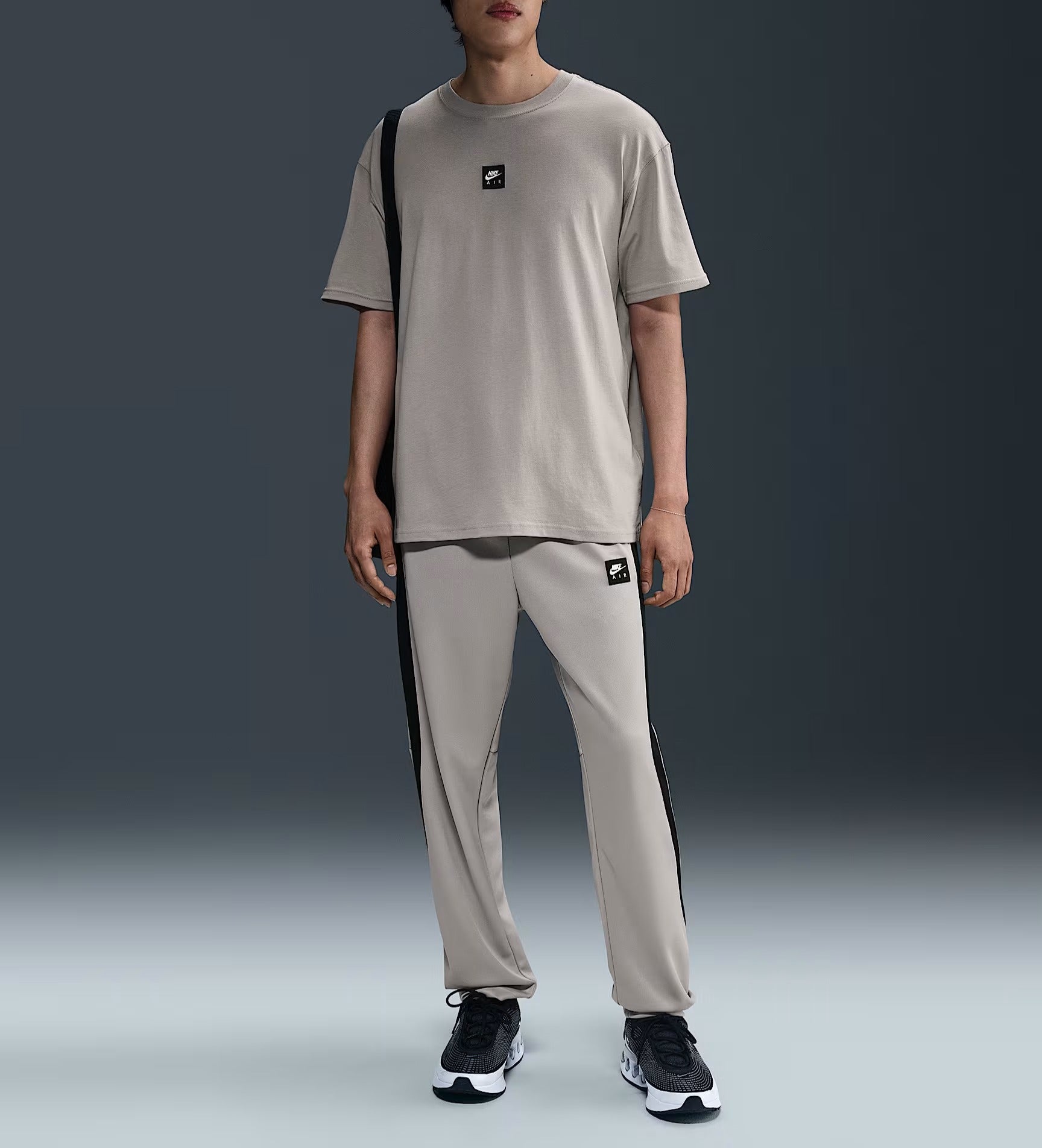 Person wearing a beige t-shirt and pants with black accents on a gradient background